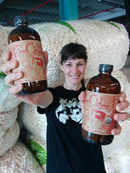 Me with Unsweetened Fire Cider in front of a wall of food starch packing peanuts (yes, they are biodegradable!)